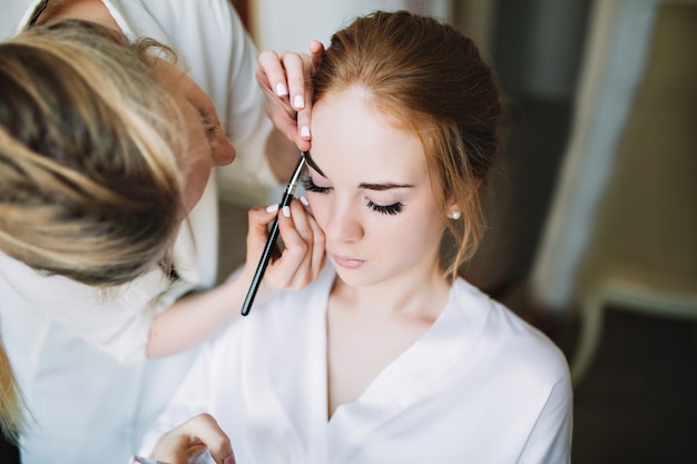 Portrait preparation of bride in the morning before wedding. artist makes makeup and she keeps eyed closed Free Photo