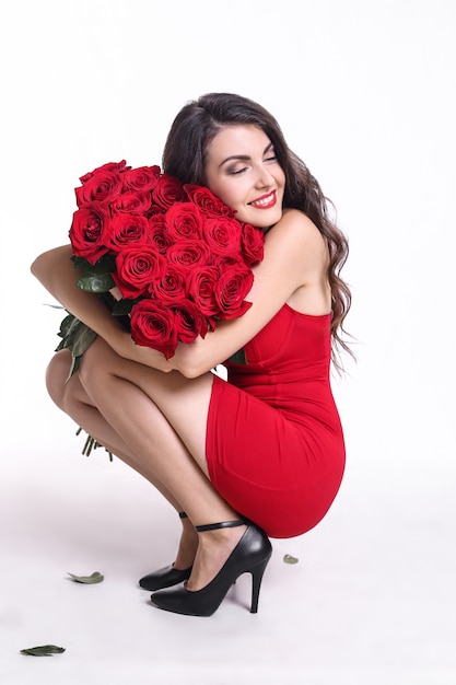Portrait of a pretty young woman dressed in red dress holding bouquet of roses isolated over white background Premium Photo