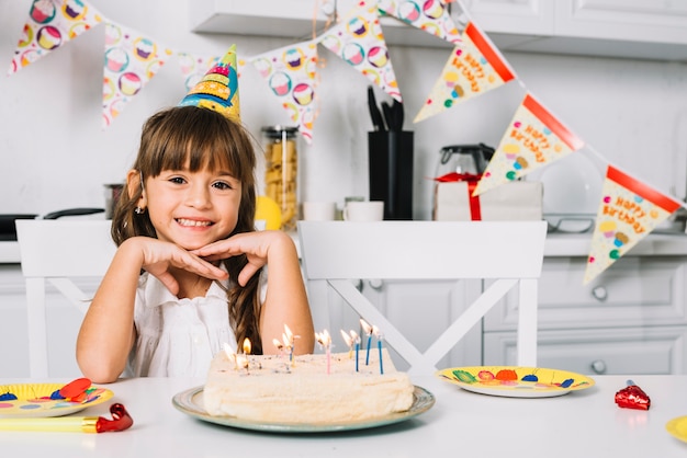 Portrait of a smiling birthday girl sitting at table with birthday cake Free Photo