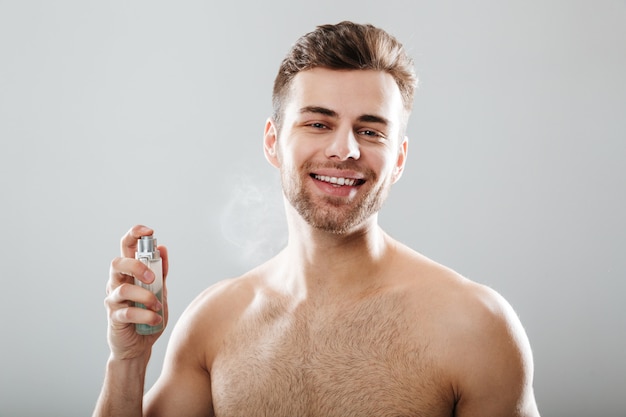 Portrait of a handsome half naked man spraying perfume 