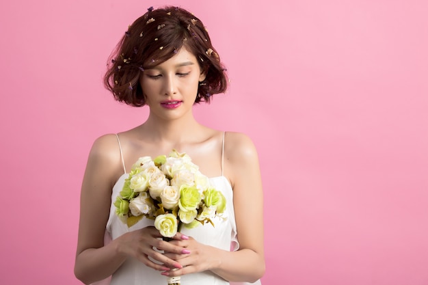 Portrait of a smiling playful cute woman holding flowers isolated on pink Free Photo