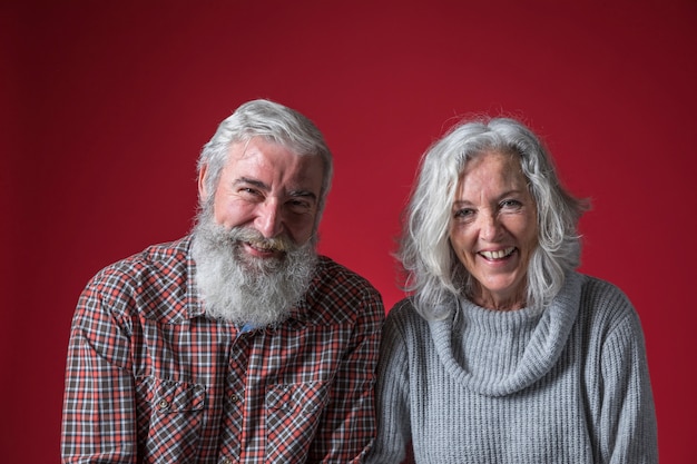 Portrait of smiling senior couple with grey hair against red background Free Photo