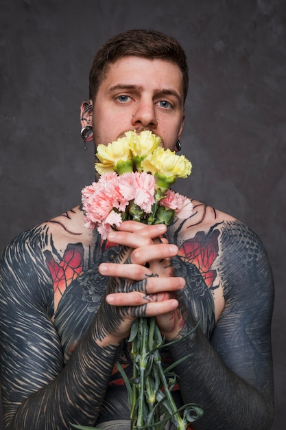 Ritratto Di Un Tatuaggio E Piercing Giovane Uomo Che Tiene Il Fiore Di Garofano In Mani Unite Foto Gratis