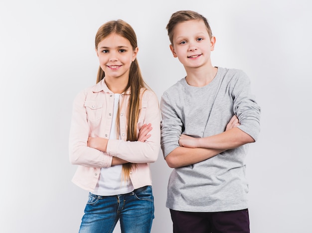 Portrait of two smiling boy and girl with their arms crossed looking to camera against white background Free Photo