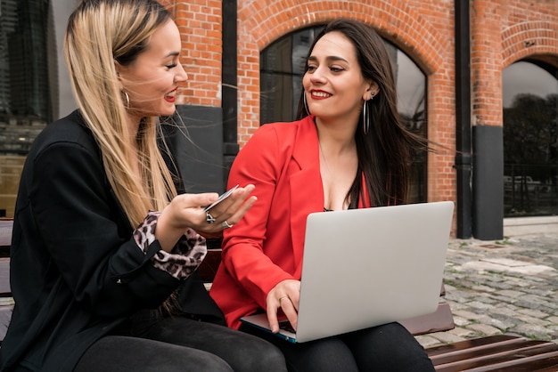 Portrait of two young friends shopping online with credit card and laptop while sitting outdoors Premium Photo