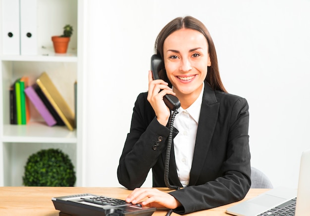 Portrait of a young businesswoman talking on telephone looking at camera Free Photo