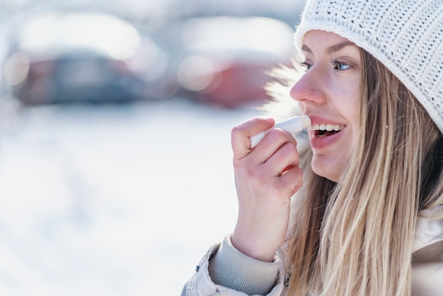 Premium Photo | Portrait of young female applying lip balm in winter.