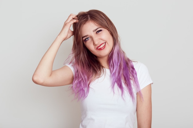 Portrait of young female in whiter casual style t-shirt scratching her hair from dandruff and irritation, suffering from lice, frowning face, isolated over grey background. Free Photo