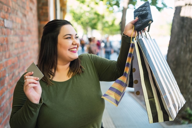 Portrait of young plus size woman holding a credit card and shopping bags outdoors on the street. shopping and sale concept. Free Photo