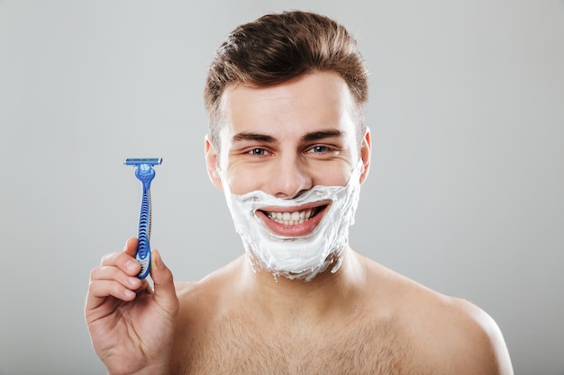 Positive Emotions Of Young Attractive Guy During Shaving With Razor In