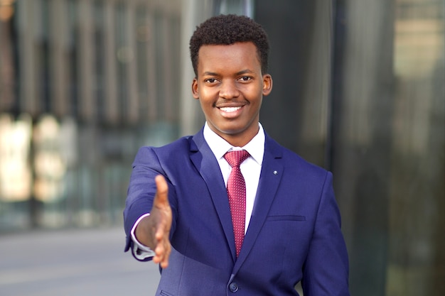 ポジティブな男性 フォーマルなスーツ を着たビジネスマンが提案し 手を差し伸べ ビジネスハンドシェイクのための手のひら 挨拶 開いた手を持つ若い黒人アフリカ系アメリカ人の男 プレミアム写真
