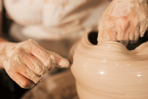 Free Photo | The potter aligns the wet clay pot with thread on the ...