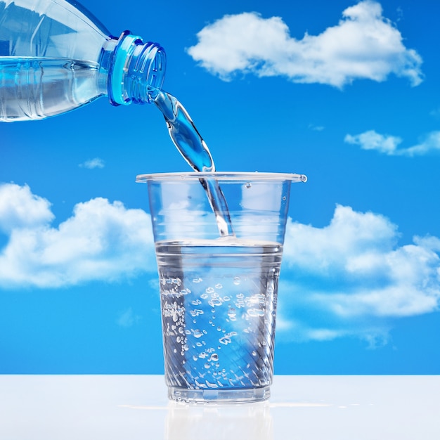 雲のある青い空を背景に ペットボトルからガラスに飲料水を注ぐ プレミアム写真