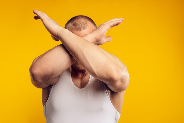 白いシャツを着て 腕を組んで 孤立した黄色の壁の上に立っている筋肉質の男性の肖像 プレミアム写真
