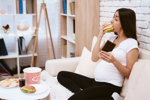 Premium Photo | Pregnant girl eating hamburger and sitting on couch.