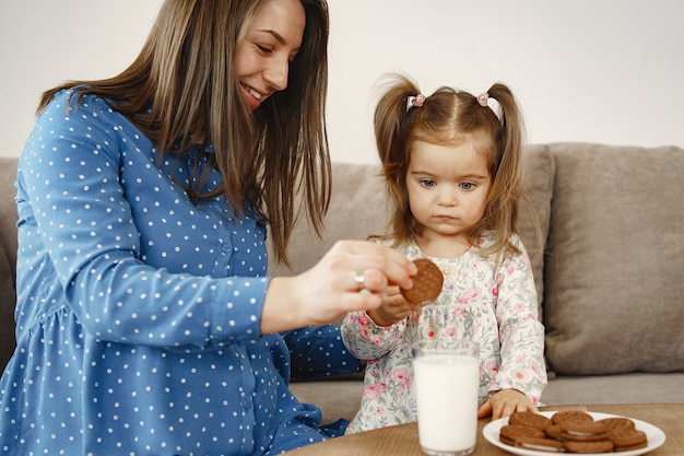 ドレスを着た妊娠中のお母さん 女の子はミルクを飲みます ママと娘はクッキーを楽しんでいます 無料の写真