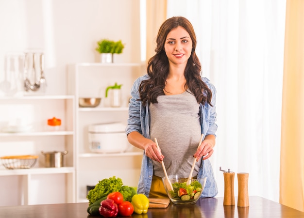 Pregnant woman cooking salad in the kitchen at home Premium Photo