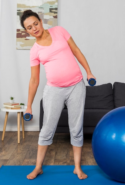 ボールとウェイトを使用して自宅でマットの上で運動している妊婦 無料の写真