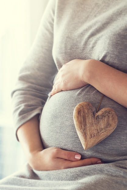 Pregnant woman holding a heart while touching her belly Free Photo
