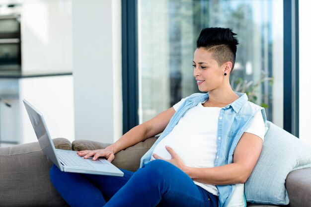 Pregnant Woman Using Laptop While Relaxing On Sofa In Living Room