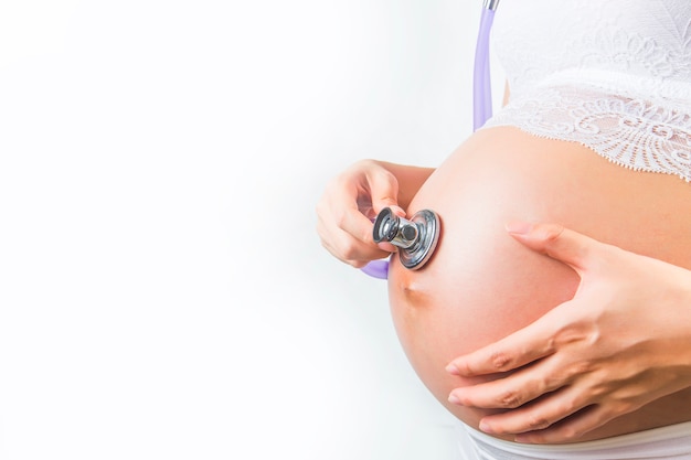 Pregnant woman using stethoscope examining on her baby in her belly Free Photo
