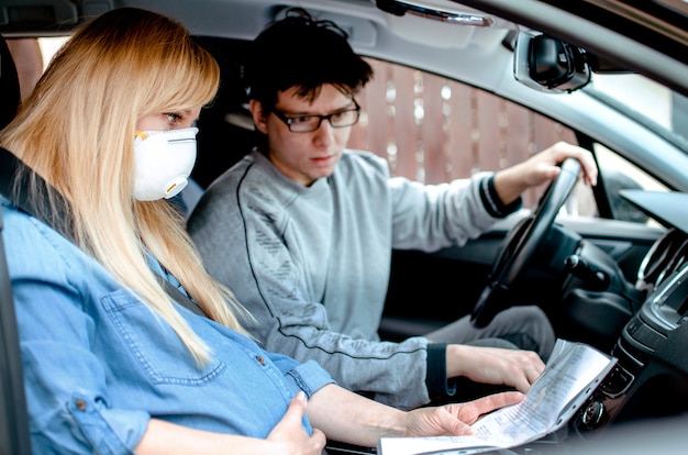 夫と一緒に病院に運転する車で陣痛のある防護マスクをした妊婦 コロナウイルスのパンデミックの状況で出産 プレミアム写真