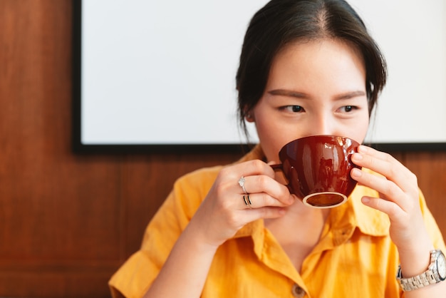Premium Photo | A pretty asian woman wearing a yellow shirt is drinking  coffee in the cafe with happy eyes.