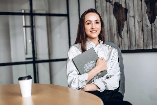 Pretty brunette with documents in her and cups of coffee, working in the official Premium Photo