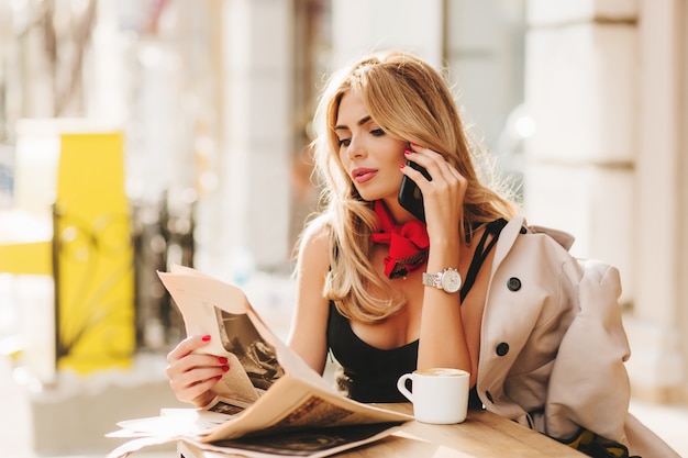 Free Photo Pretty Busy Lady Posing In Outdoor Restaurant With Newspaper Reading It With Interest On Blur Background