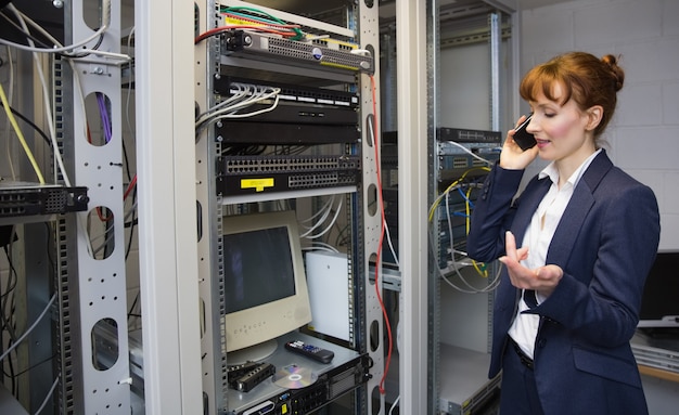 Pretty computer technician talking on phone beside open server Premium Photo