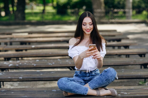 Pretty Girl Typing On Her Phone Sitting On The Bench In A Park Photo