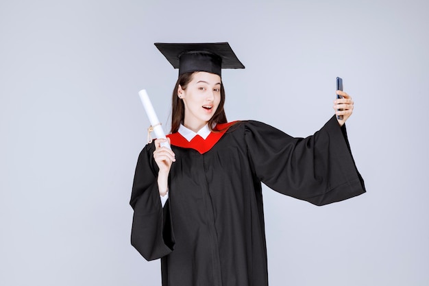 Premium Photo | Pretty graduate student in gown taking selfie. high ...