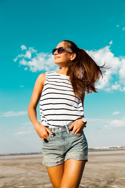 Free Photo Pretty Happy Girl In A Striped T Shirt And Jeans Shorts Posing With Glasses In The Beach