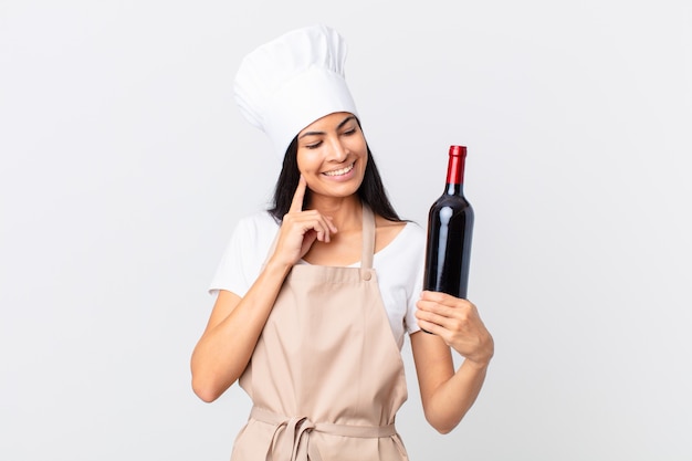Premium Photo Pretty Hispanic Chef Woman Smiling Happily And Daydreaming Or Doubting And Holding A Bottle Of Wine