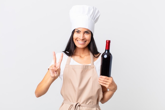 Premium Photo Pretty Hispanic Chef Woman Smiling And Looking Friendly Showing Number Two And Holding A Bottle Of Wine