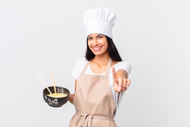 Premium Photo Pretty Hispanic Chef Woman Smiling Proudly And Confidently Making Number One And Holding A Noodle Bowl