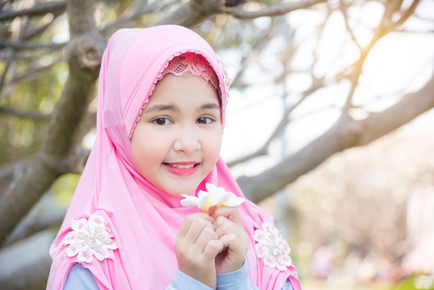 Pretty muslim girl standing under a tree and holding white flower with smiles. Premium Photo