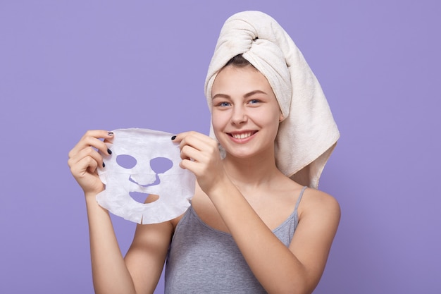 Pretty young female holds beauty mask in hands, being ready to apply it on face for rejuvenating Free Photo