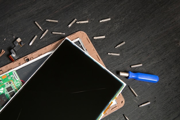 Process of pc tablet device repair near screwdriver and bit on black wooden surface disassembled Premium Photo
