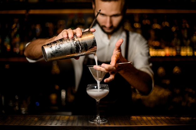 Professional bartender pouring a white cocktail from the