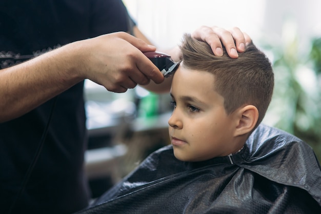 プロの美容師は 小さな男の子の髪を縁取るためにバリカンを使用しています プレミアム写真