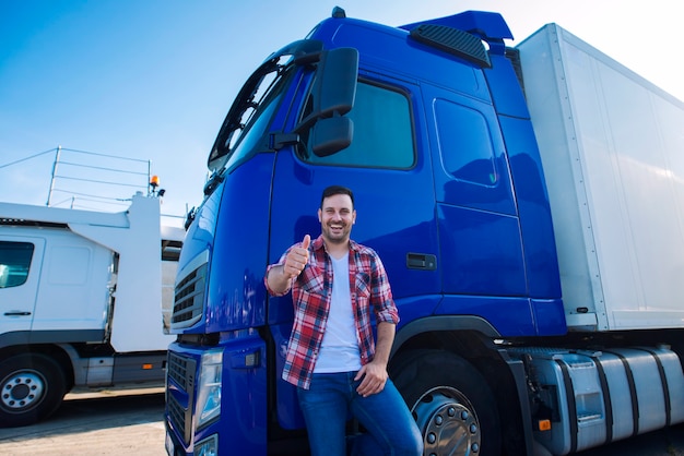 Professional truck driver in front of long transportation vehicle holding thumbs up ready for a new ride Free Photo