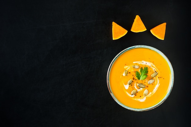 Pumpkin and carrot soup with cream, pumpkin seeds and parsley on dark scratched background. Premium Photo