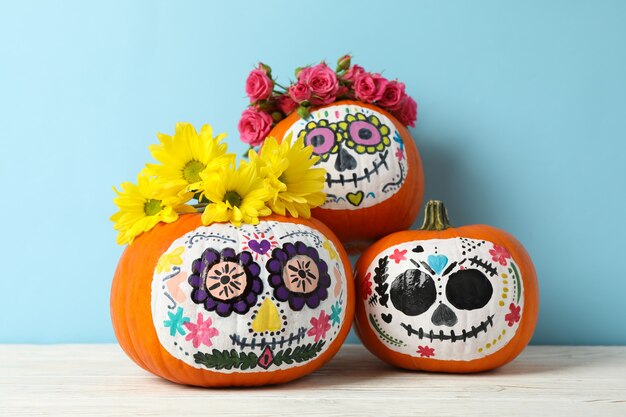 Premium Photo | Pumpkins with catrina skull makeup and flowers on blue wall