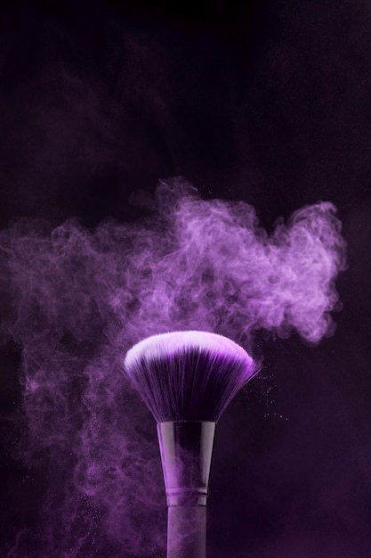 Purple burst of makeup powder and brush on dark background Free Photo