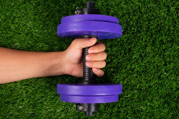 Premium Photo | Purple dumbbell in hand on green grass