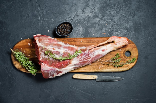 Raw leg of lamb on a wooden chopping board. rosemary, thyme, black pepper. Premium Photo