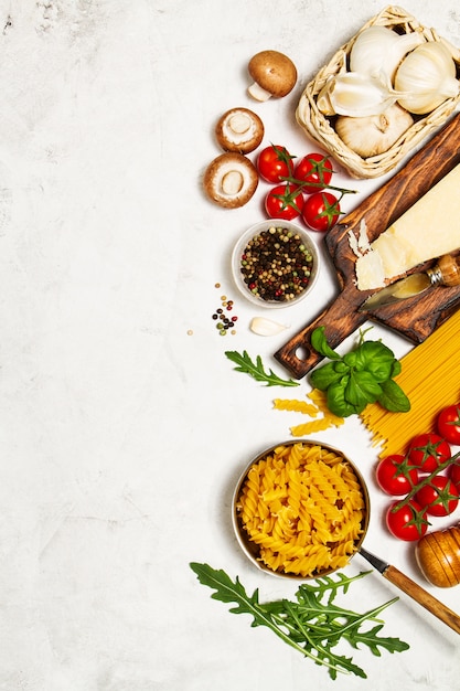 Raw pasta with tomatoes and spices with a cutting board with cheese Premium Photo Raw pasta with tomatoes and spices with a cutting board with cheese Premium Photo