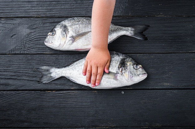 子供と生のドラドまたは鯛魚は黒い木製のテーブルでそれを引き渡す プレミアム写真