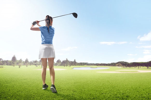 Rear view of asian woman on long drive swing with wood club in the golf course with sand bunkers, pond and trees Premium Photo